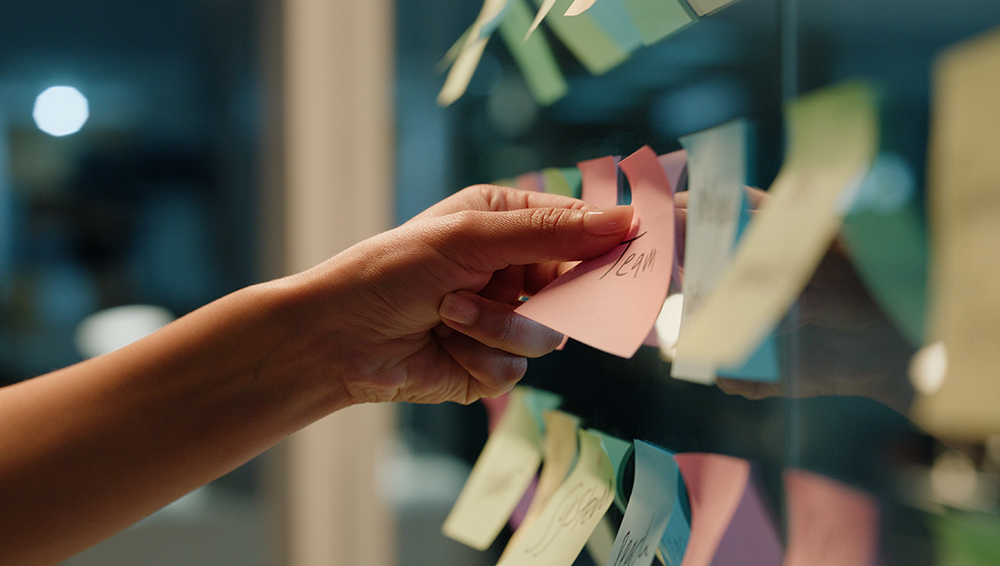 person adding a sticky note to a wall of ideas